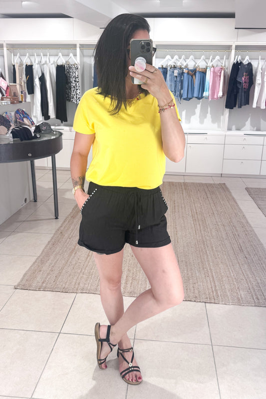Short noir taille haute porté avec un tee shirt jaune, look estival tendance SANAES
